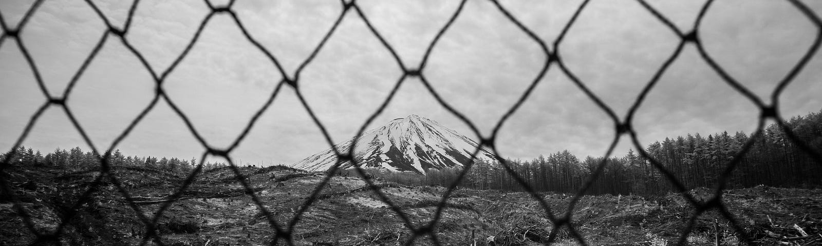 Snow capped Mt. Fuji in the distance behind a chain link fence.