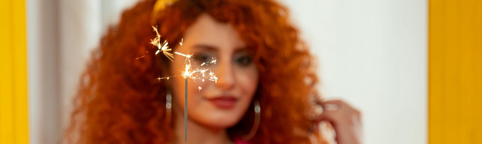 red haired girl smiling, holding sparkler over cake with flowers