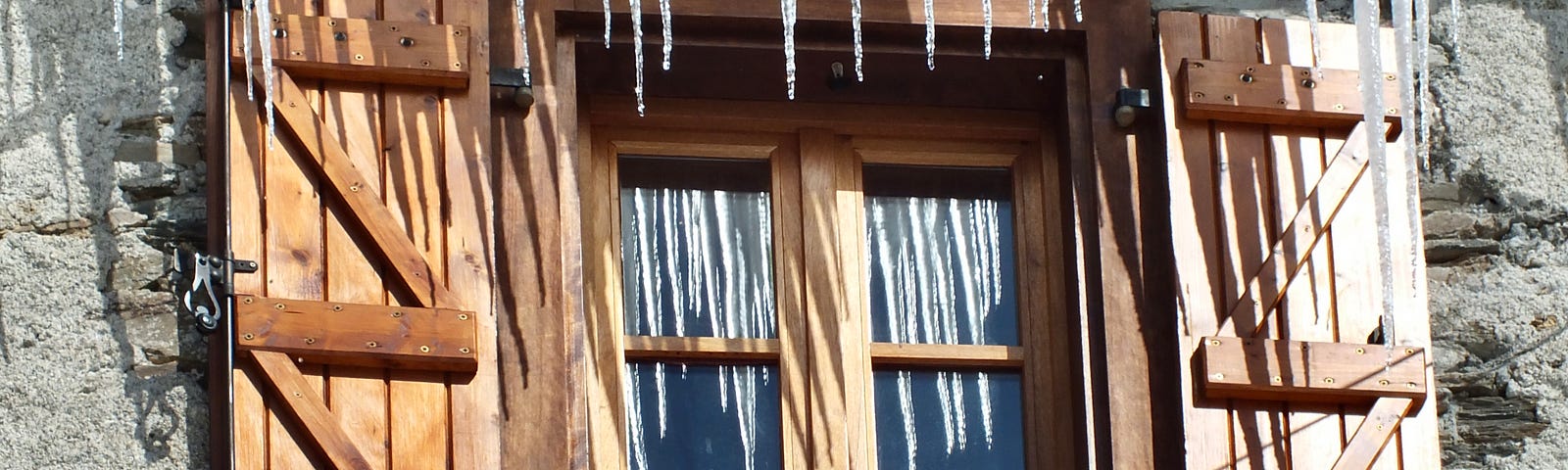 Brown wooden shutters open either side of a window, with long, thin icicles hanging from the roof.