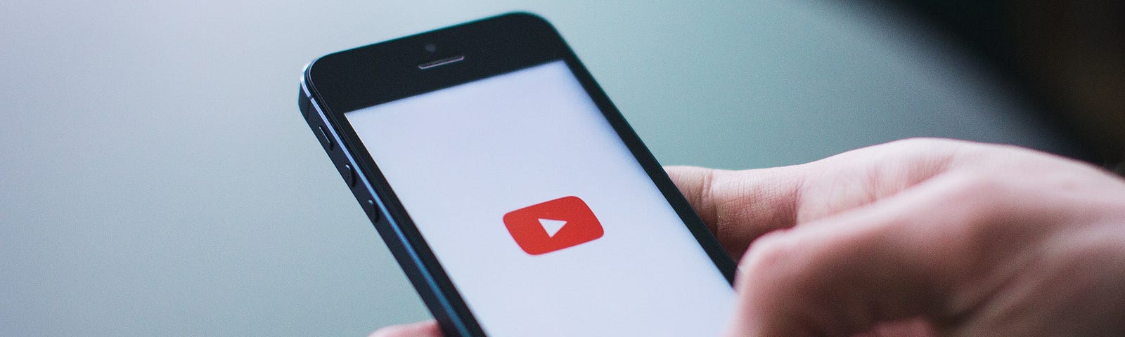 A hand holding a mobile phone with the Youtube logo on screen.