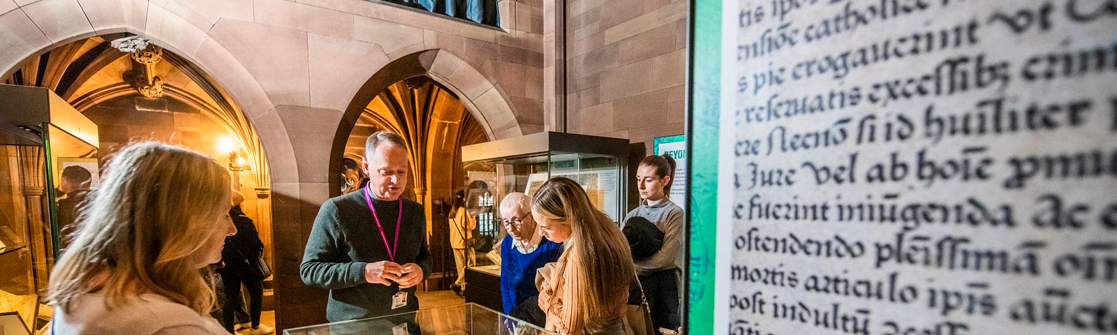 Visitors standing in the Transitions in Print exhibition, listening to a tour and examining the display cases.