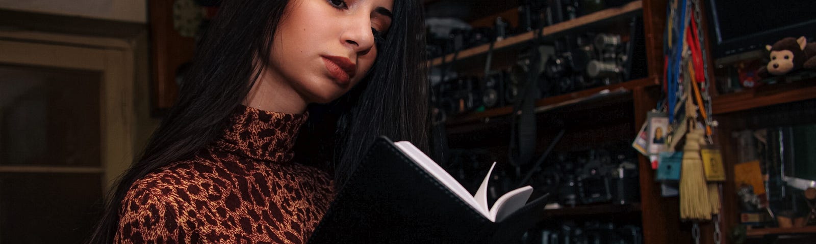 Woman reading book in dimly liy room with large wooden shelf behind her