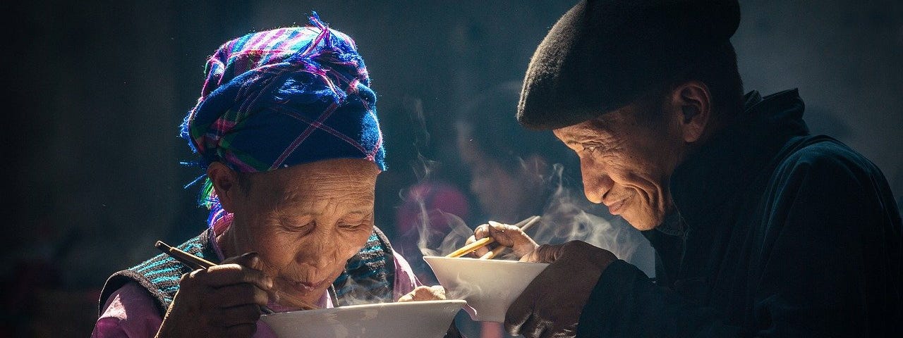 An elderly Asian couple eating with chopsticks.