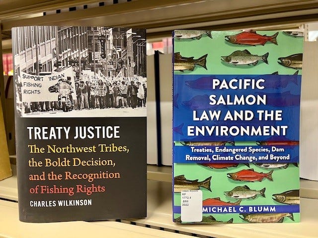 Two books sit side by side on a shelf. They are shown with their covers out. The book on the left is titled, “Treaty Justice: The Northwest Tribes, the Boldt Decision, and the Recognition of Fishing Rights.” The book on the right is titled, “Pacific Salmon Law and the Environment.”