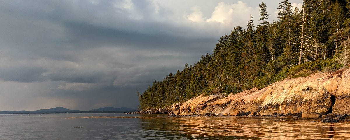 A feeling of awe is created as pink granite cliffs are highlighted by the afternoon sun as an ocean storm retreats into the distance.