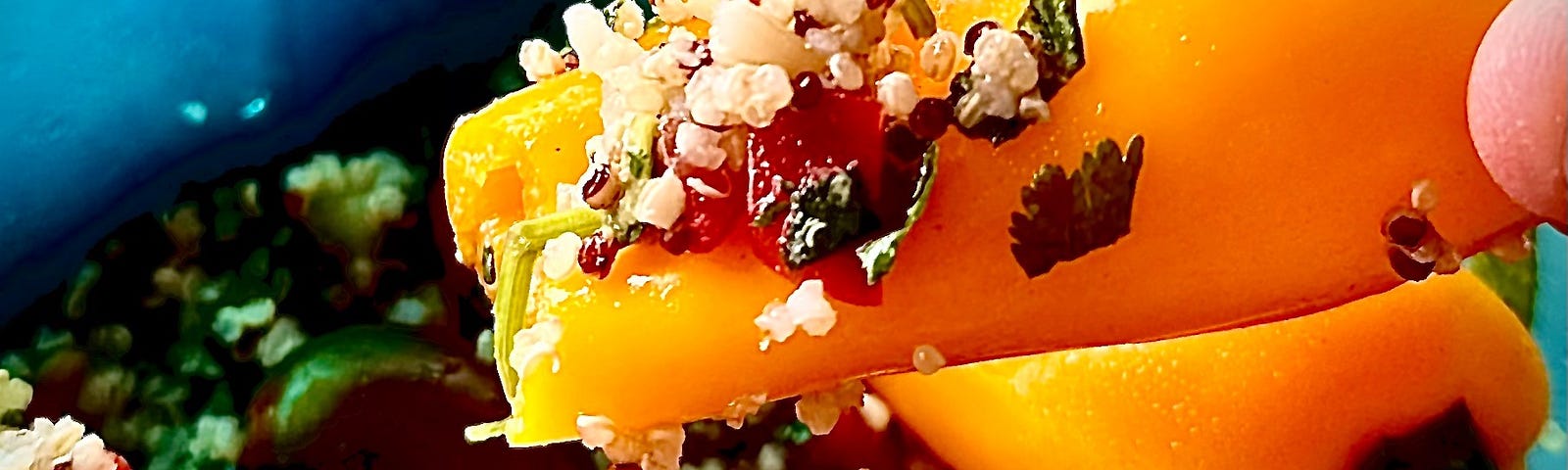 Tupperware box with quinoa salad, tomatoes, and a hand holding a small bell pepper with some salad on it as a spoon.