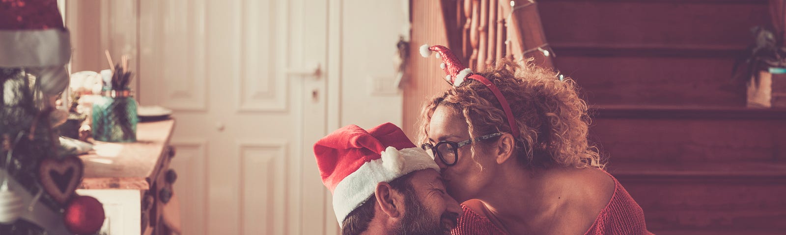 A couple surrounded by holiday decorations kiss happily at home.