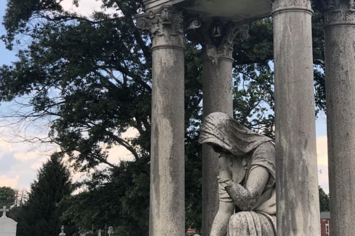 A sculpture of a mourning woman, robed and looking down, in a cemetery