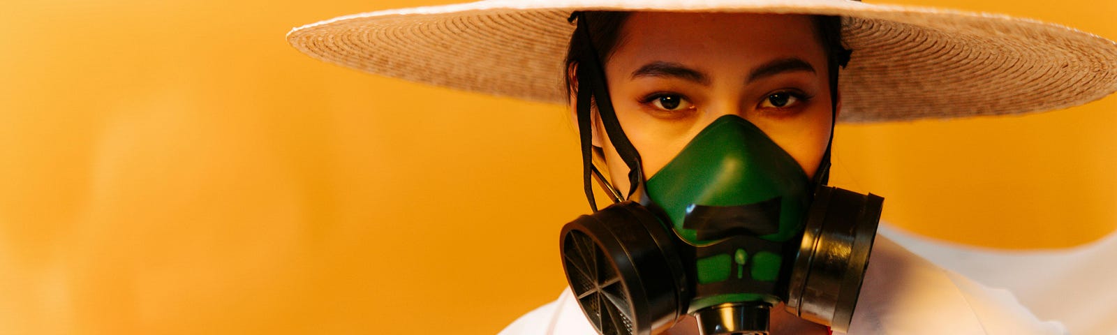 A woman is wearing a black and green respirator against a solid yellow backdrop