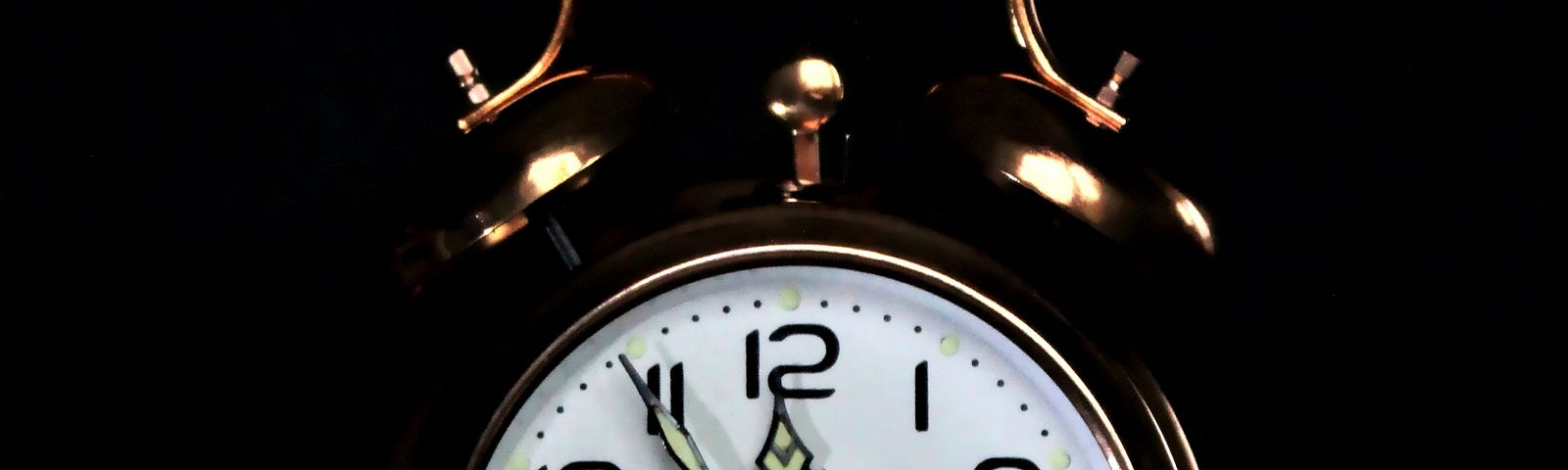 An analog clock set to five minutes before midnight against a black background.