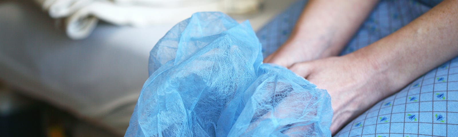 A man in a blue hospital gown sitting on a hospital bed and holding a hair net.