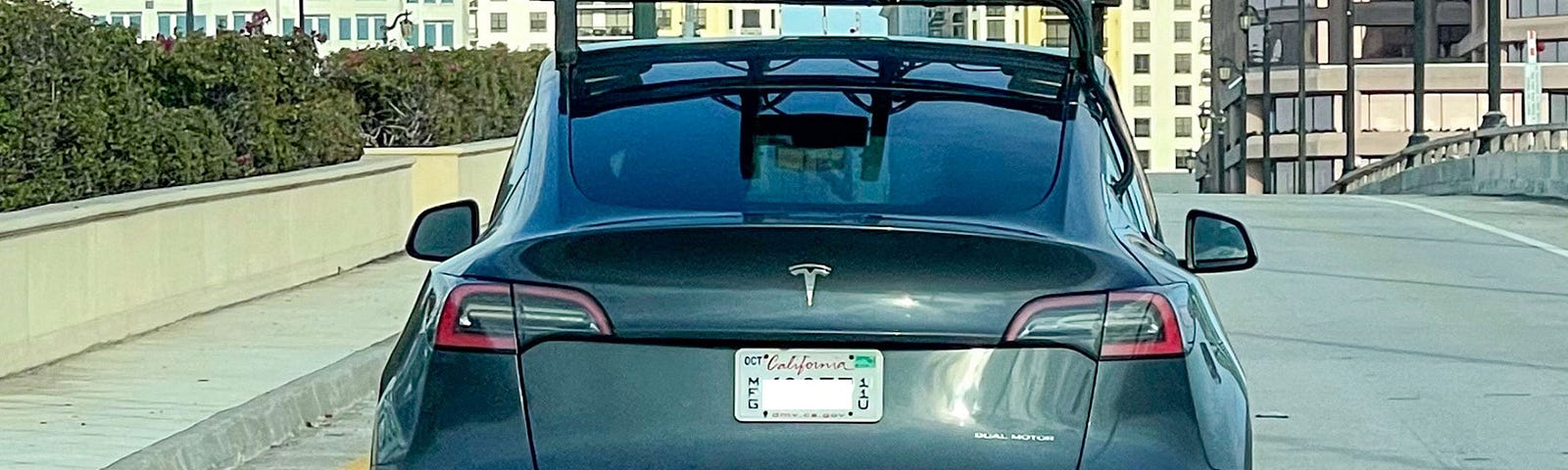 A grey Tesla seen from the rear with a large roof-mounted rack holding a lidar sensor array.