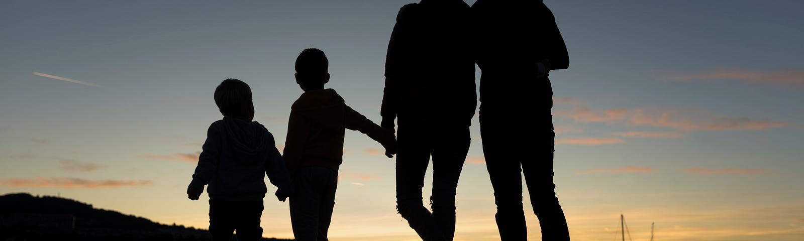 The silhoutte of a family holding hands at sunset.