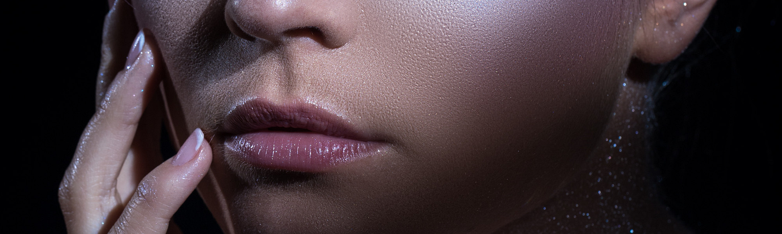 A close-up portrait of a woman adorned with sparkling makeup and glitter, showcasing dramatic eye embellishments and a shimmering bracelet.