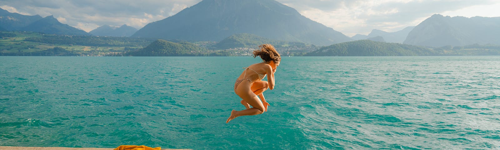 A woman jumping into a lake in the Swiss Alps in summertime.