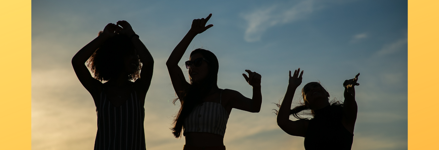 Silhouettes of three people dancing in front of a blue sky.