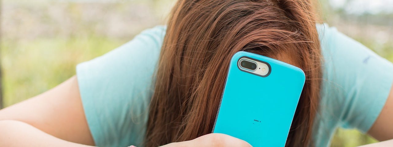 IMAGE: A teen girl hiding her face behind a smartphone