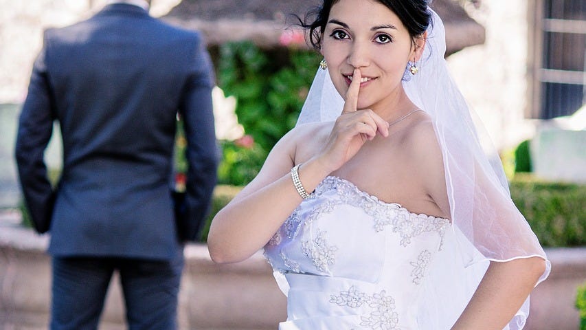 A bride with her finger over her lips to keepeveryone quiet.