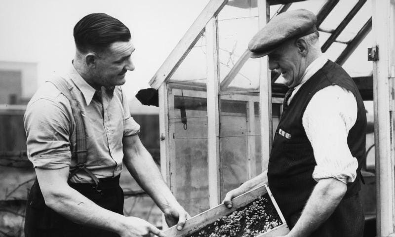 Two men from the 1940s discuss the farm products one of them is holding