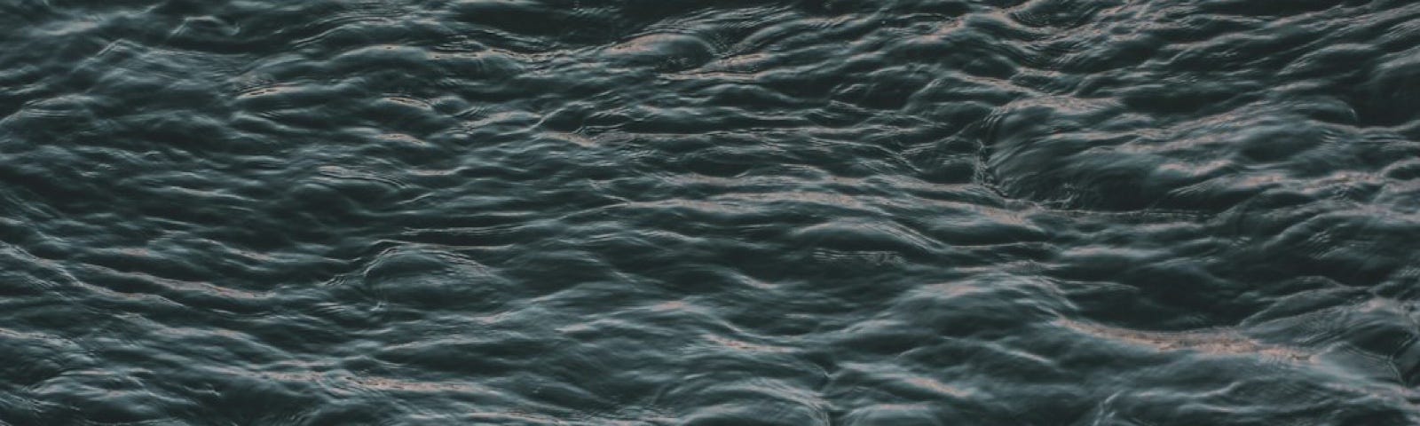 a serene surface of water, characterized by gentle ripples and a deep, dark hue.