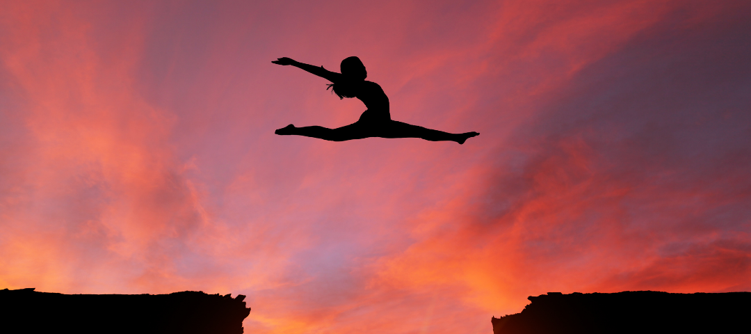 A dancer leaping over two cliffs with the sun coming up through the gap.