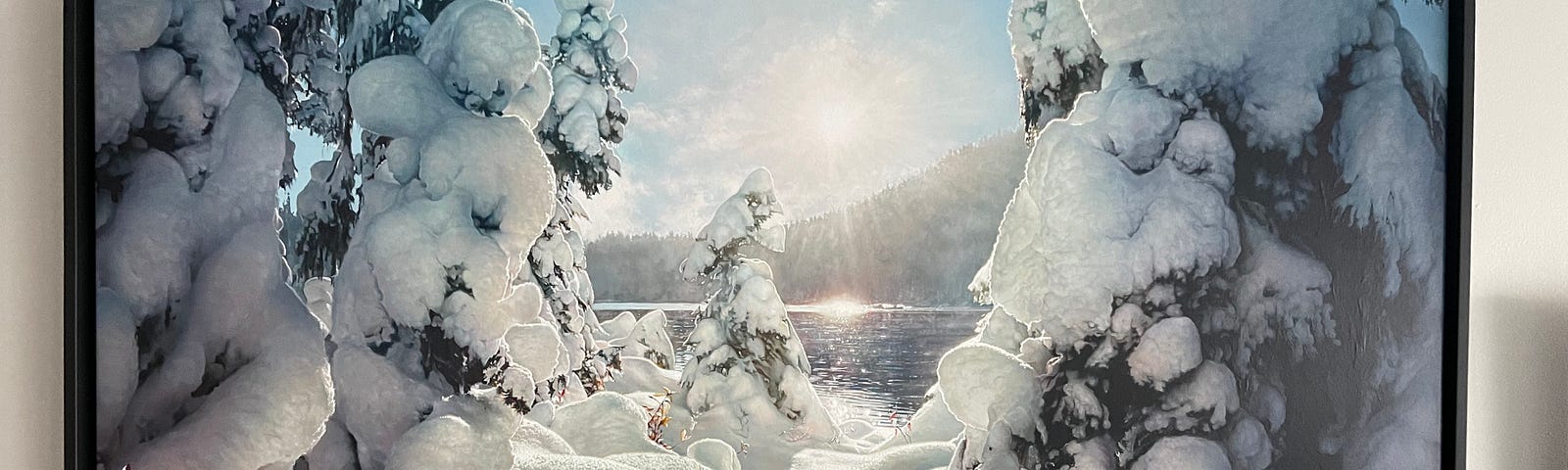 Sun reaches around a mountain reflecting on a lake amidst snow-laden trees.