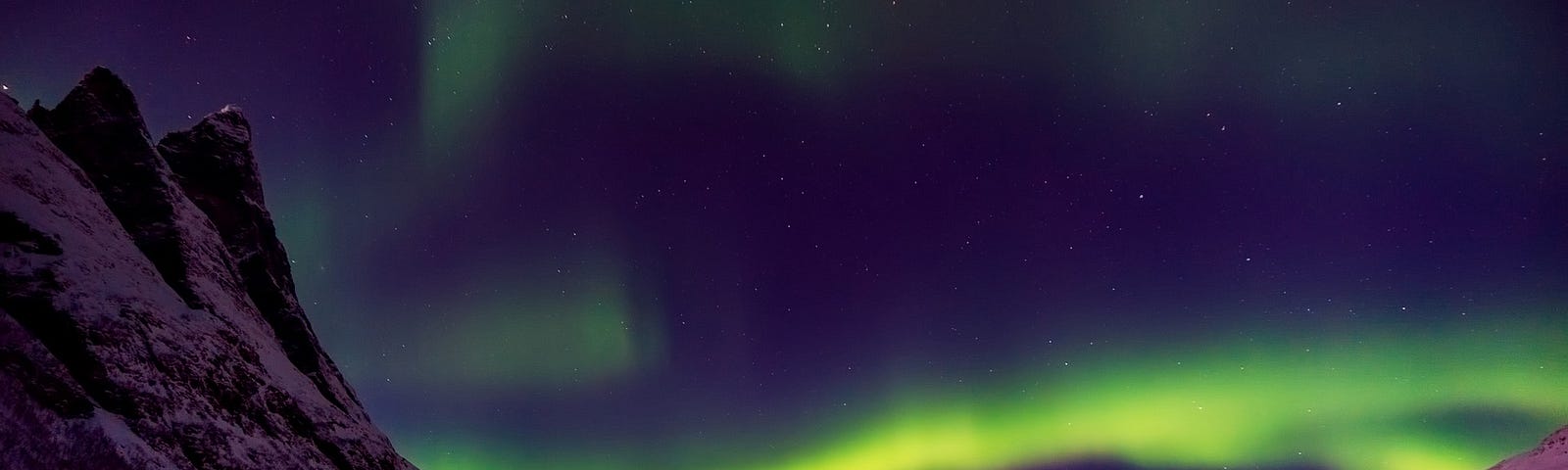 A view through a mountain valley of the northern lights, lighting the sky with a spectrum of colors