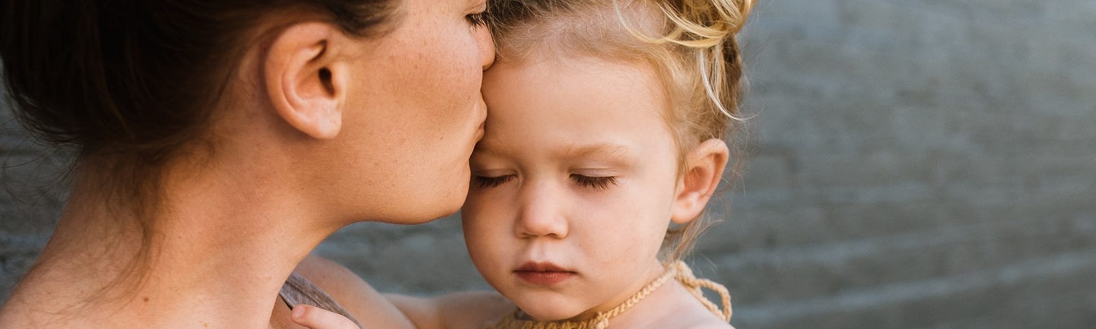 Woman kissing child on the forehead, both with eyes closed