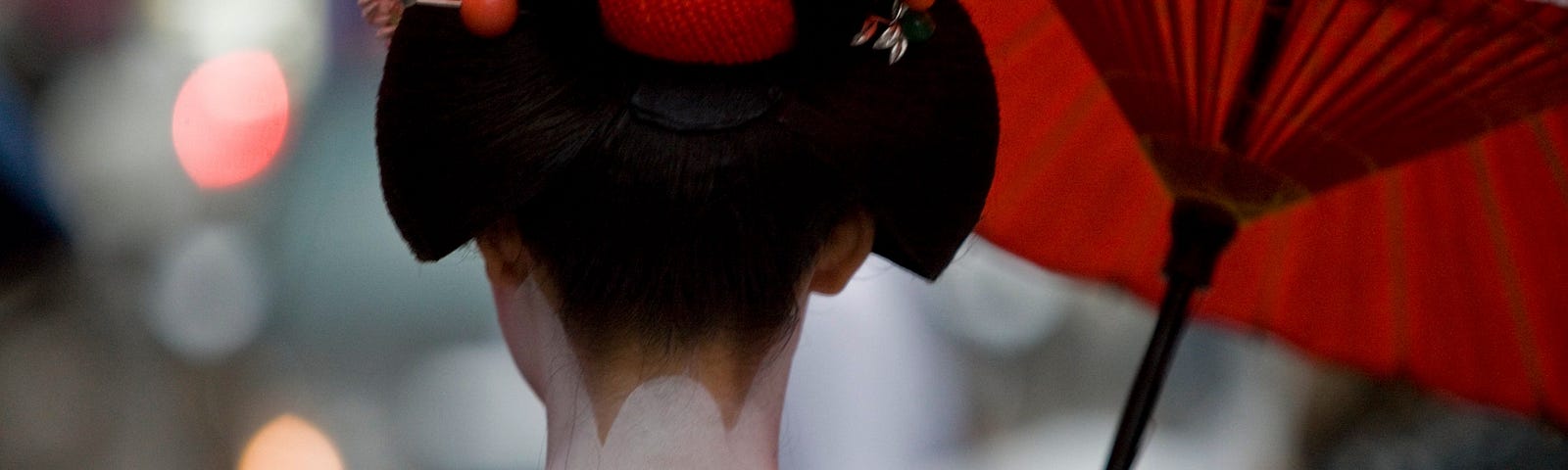 Back view of a geisha showing her white neck and top of her back, hair up and decorated with accessories.