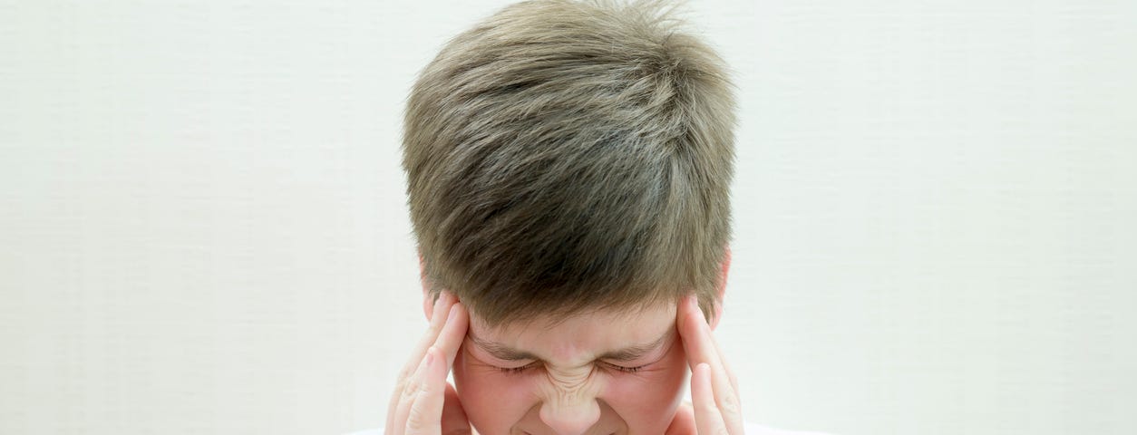 young boy holding both temples, squiting eyes due to a headache