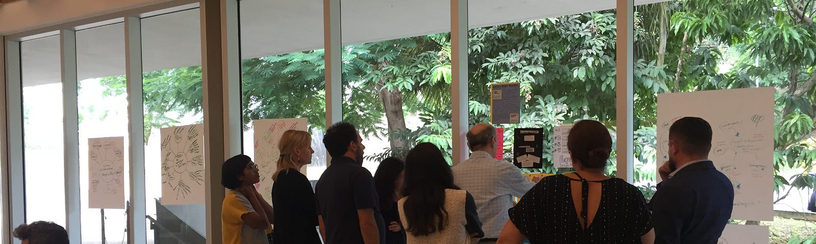 Image of Equity Design participants grouped around posters on a glass wall to check out each other’s work.