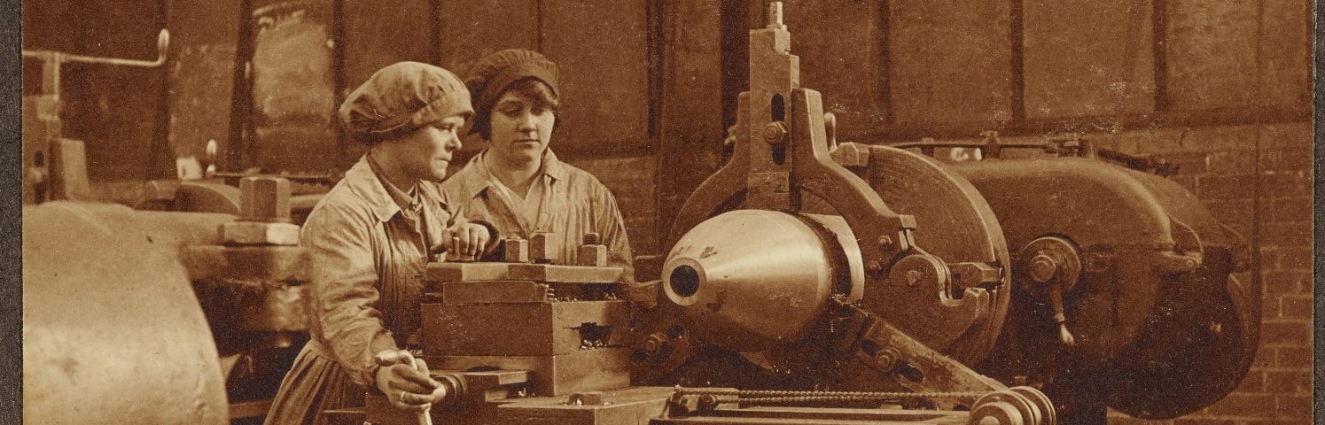 Sepia photograph of two women shell makers, operating heavy machinery to finish off an 11 inch metal shell.