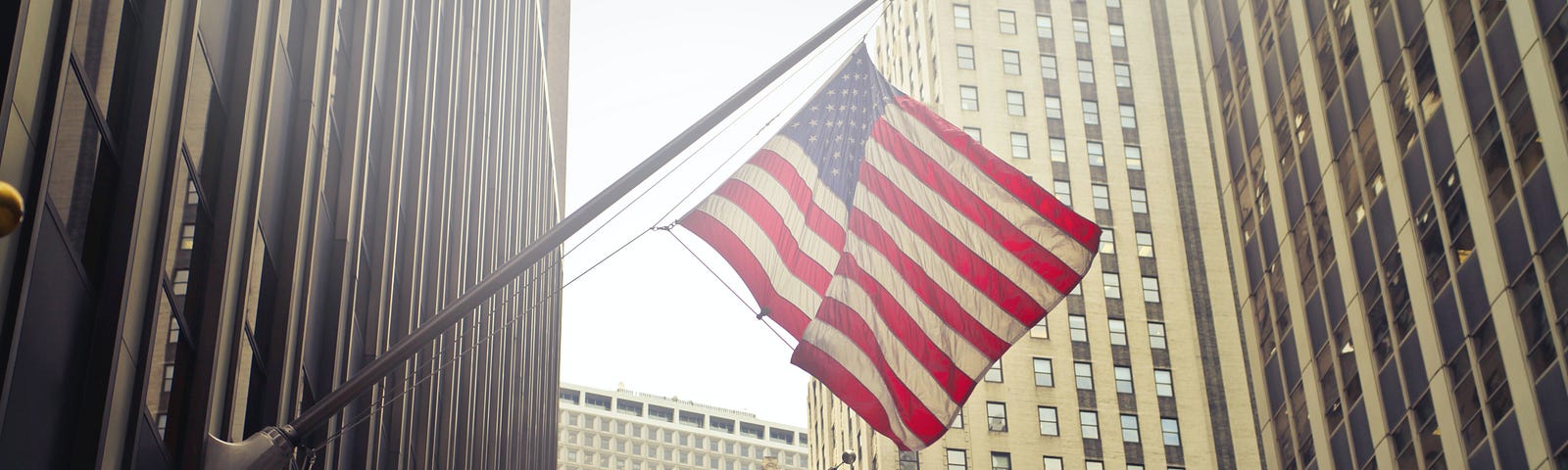 Two flags hang from poles coming off of large, corporate buildings.