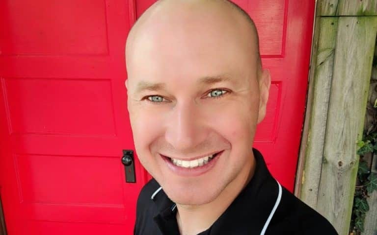 A very bald christopher kokoski standing in front of a very red door.