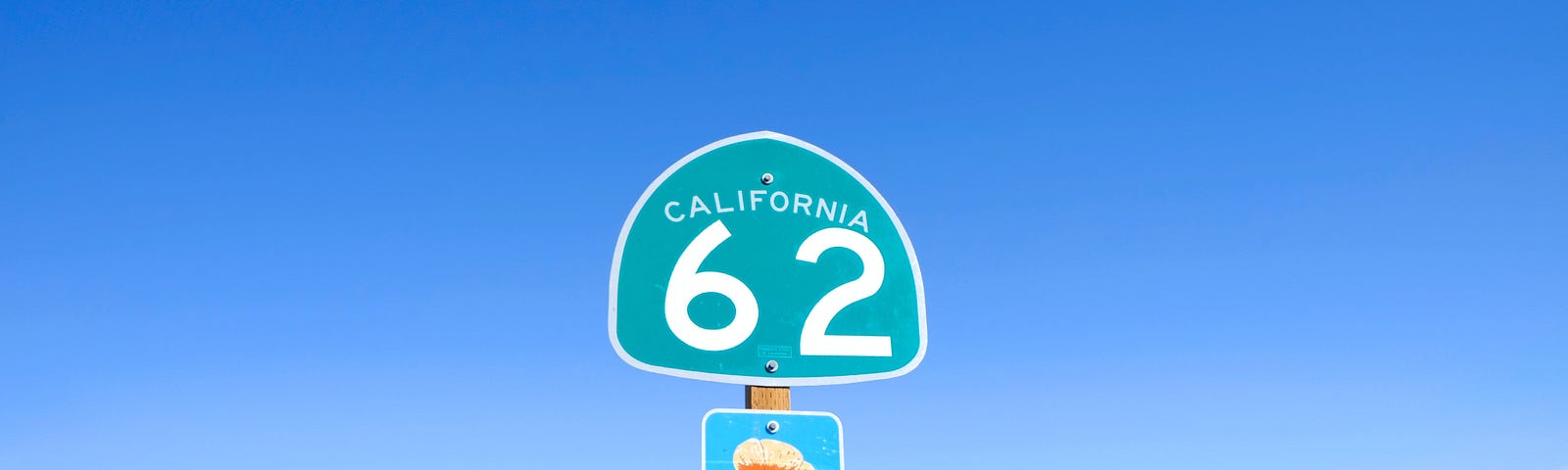 California Highway Sign with number 62 displayed. Desert and scrub displayed in the background to the right, with the highway long perspective shown to the left.