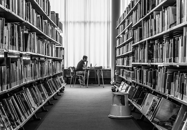 A man sitting at a table at the end of a row of books in a library.