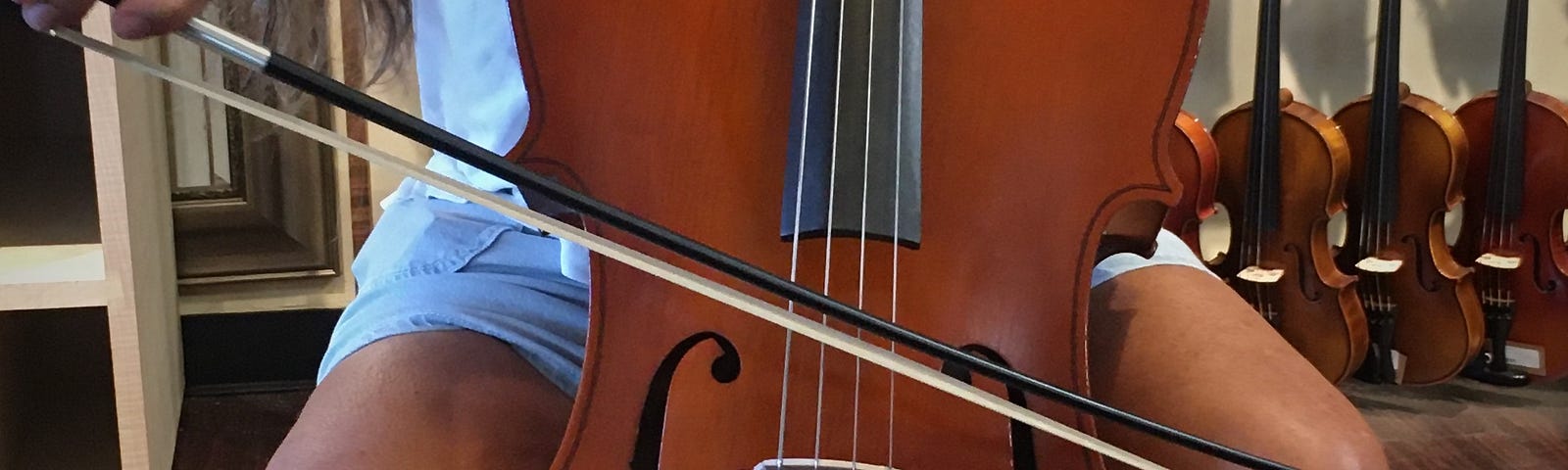 A close up color photo of a cello being played, cropped to show the instrument’s finger board and bowing hand of the musician.