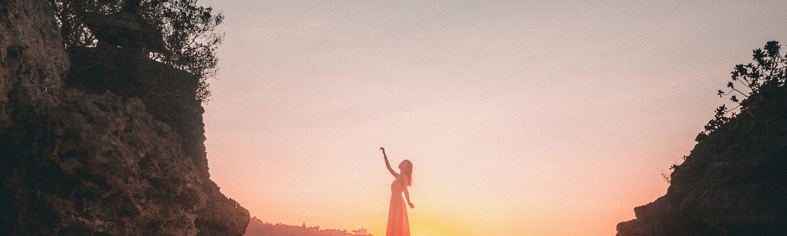 Woman standing on a rock platform on the beach with a sunset behind her