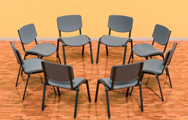 A circle of 8 chairs placed on a wooden floor.