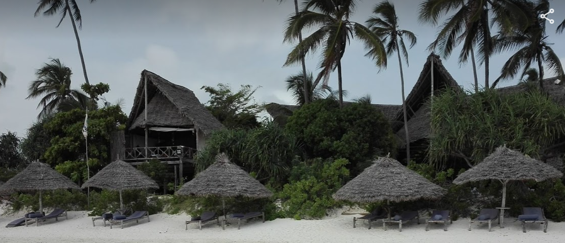 White sandy beach with Zanzibar-style thatched beach umbrellas and towering A-Frame thatched lodge fringed with palm trees