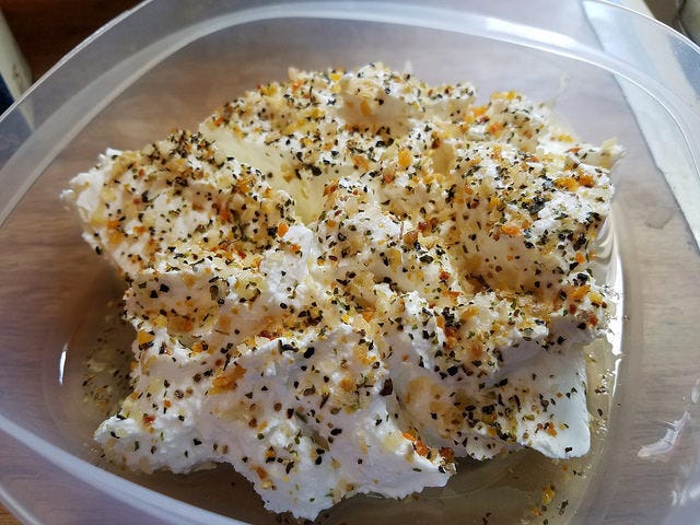 Homemade labneh made from Greek yogurt in a plastic container with olive oil and Trader Jore’s Tewnty-One Seasoning Salute spice blend sprinkled on top.