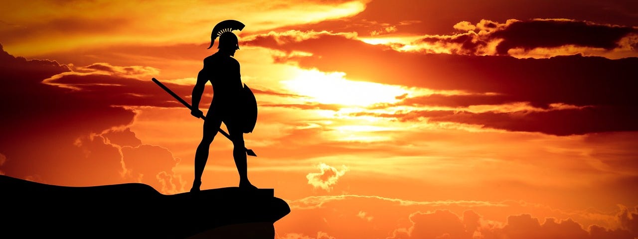A male warrior stands on a ledge facing the day as it dawns.