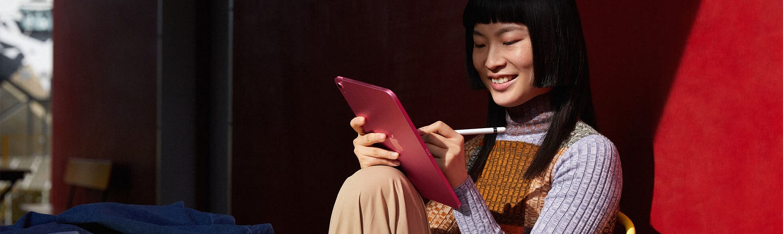 A person sitting on a desk using Apple Pencil on a pink iPad.