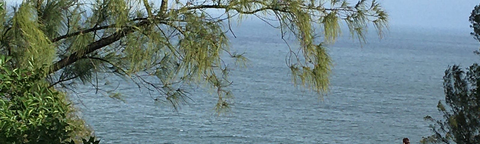 An outdoor view of the sea, on the island of a catholic retreat camp. A statue of St. Mary on the lower left and a girl glazing to the sea on a white open platform on the upper right.