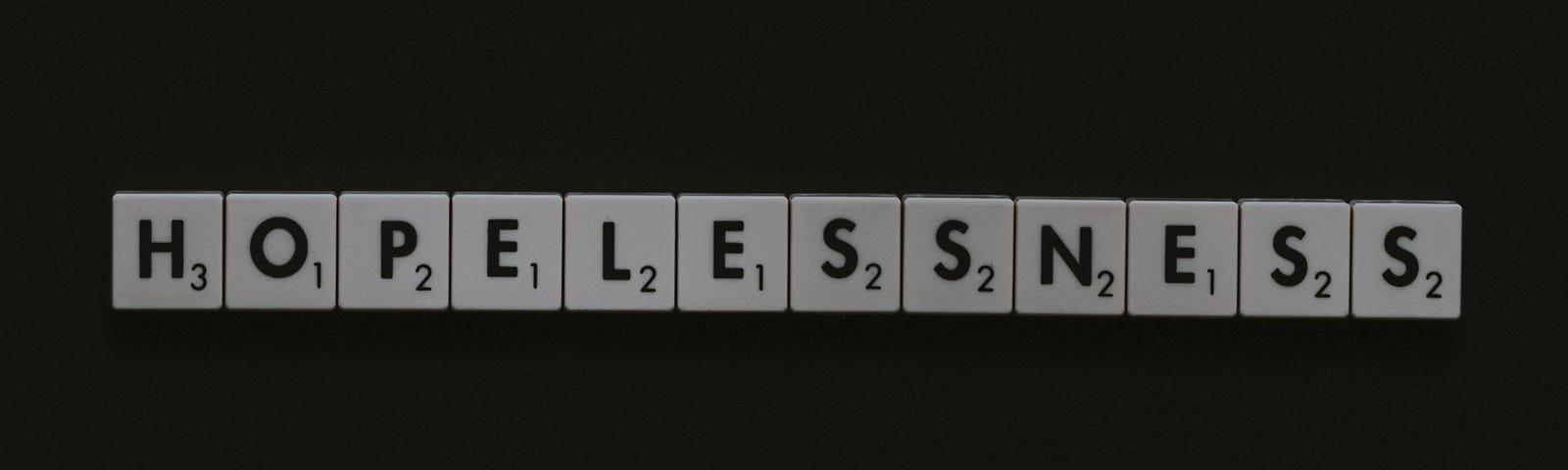 The word “hopelessness” spelled out in Scrabble tiles on a black backgrouns.