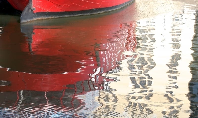 Abstract photograph of red boat in water with ripples and light reflection, for healing