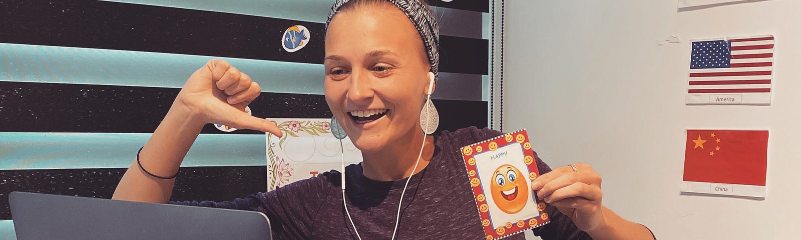 Girl sits at a high rise table with a computer in front of her. She is pointing to herself while holding a happy face.