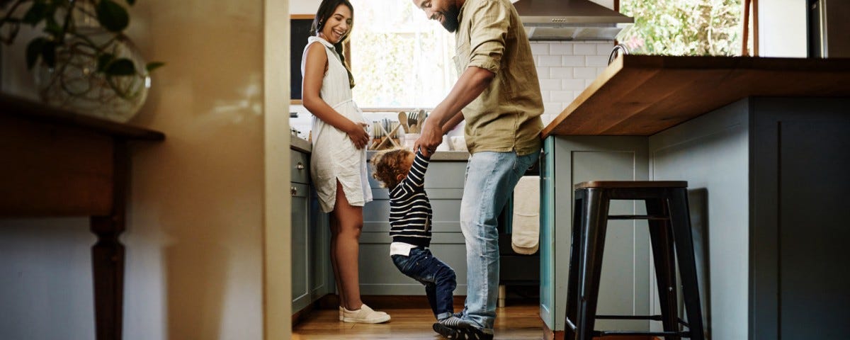 Una familia con niños juega dentro de la casa mientras un perro está recostado en el piso de la cocina.