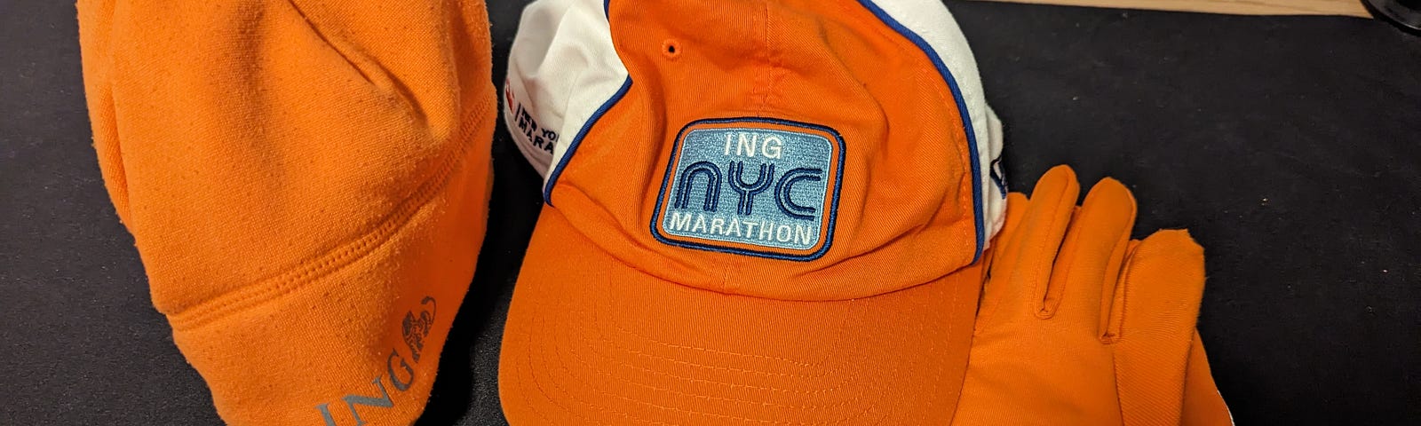 Bright orange winter hat, gloves, and baseball cap from the NYC Marathon