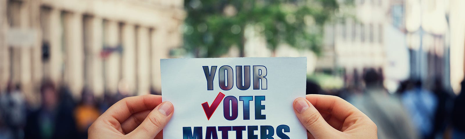 A picture of two hands, holding a small sign reading “YOUR VOTE MATTERS.”